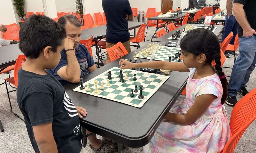 A young CHESSKLUB student focused on making a move in a chess game with peers.