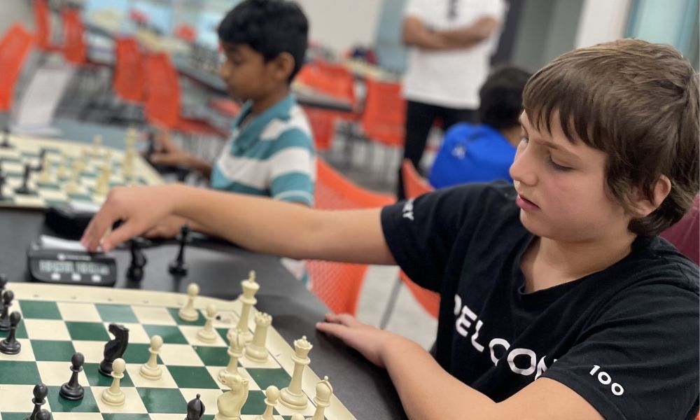 A CHESS KLUB student thoughtfully makes a move on a chessboard at a competitive youth chess event.